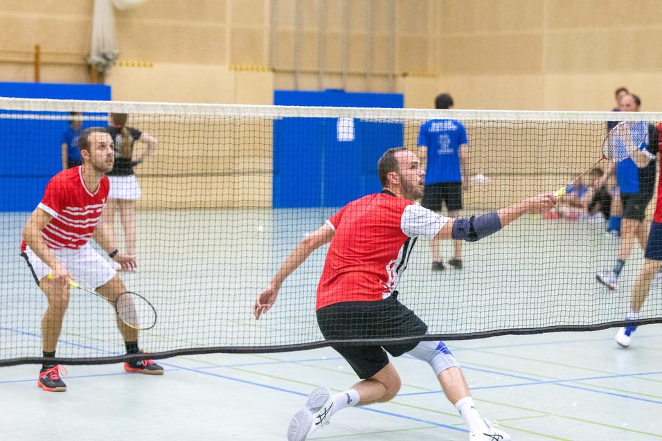 Zwei Badmintonspieler in roten Trikots stehen auf dem Feld und spielen einen Ball &uuml;ber das Netz.