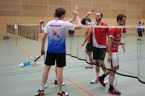 F&uuml;nf Badmintonspieler stehen auf einem Court und gratulieren sich nach einem Spiel. Netz im Hintergrund.