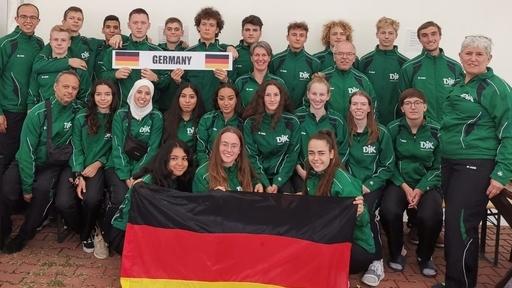 Gruppenshot von 20 Personen in gr&uuml;nen Sportjacken, halten ein Schild mit &bdquo;GERMANY&ldquo; und eine deutsche Flagge.