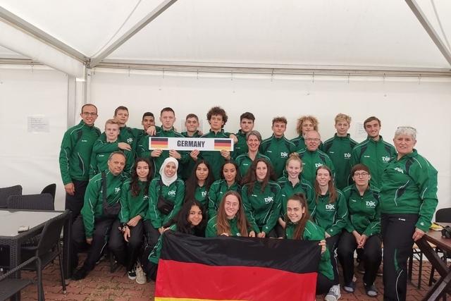 Gruppenshot von 20 Personen in gr&uuml;nen Sportjacken, halten ein Schild mit &bdquo;GERMANY&ldquo; und eine deutsche Flagge.