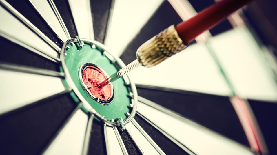 Nahaufnahme eines Dartpfeils, der im roten Zentrum einer schwarz-weißen Dartscheibe steckt.