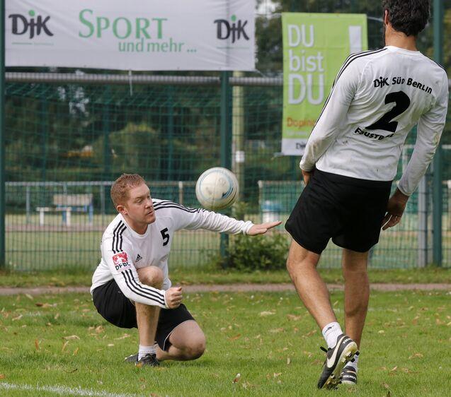 Zwei Fußballspieler trainieren im Freien; ein Spieler kniet, der andere passt den Ball.