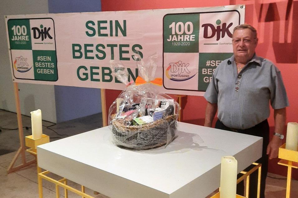 Mann steht neben einem Tisch mit einem Geschenkkorb, vor einem Banner mit dem Text &bdquo;100 Jahre &ndash; Sein bestes Geben&ldquo;.