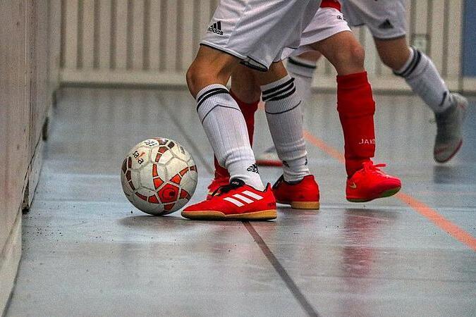 Nahaufnahme von zwei Spielern in wei&szlig;en Trikots mit roten Schuhen, die einen Fu&szlig;ball an einer Wand ber&uuml;hren.