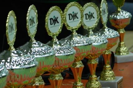 Reihe von goldenen Pokalen mit gr&uuml;n-wei&szlig;en Logos auf einer Tischplatte.