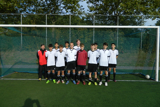 Mannschaftsfoto einer Fu&szlig;ballmannschaft in wei&szlig;en Trikots vor einem Tor auf einem Kunstrasenplatz.