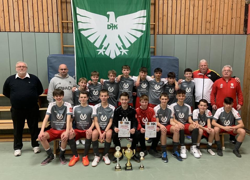 Gruppenfoto einer Jugendmannschaft mit Pokalen und Urkunden vor einer gr&uuml;nen Fahne des Vereins DHK.