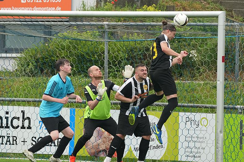 Spielszene: Ein Fu&szlig;ballspieler springt hoch, um den Ball im Torraum zu k&ouml;pfen, w&auml;hrend drei Verteidiger reagieren.