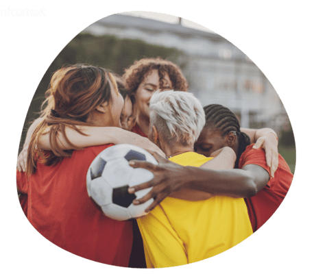 Vier Personen in Sportkleidung umarmen sich, w&auml;hrend eine Person einen Fu&szlig;ball h&auml;lt. Gemeinschaft und Freude im Spiel.