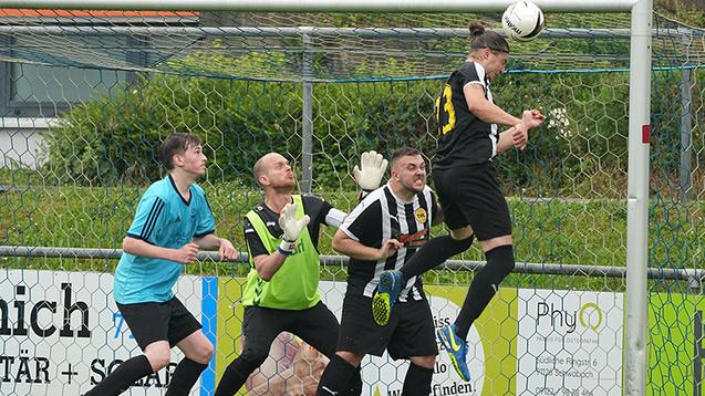 Spielszene: Ein Fu&szlig;ballspieler springt hoch, um den Ball im Torraum zu k&ouml;pfen, w&auml;hrend drei Verteidiger reagieren.
