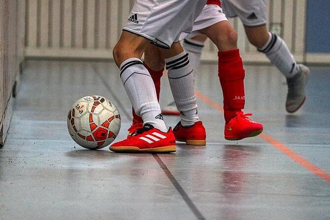 Nahaufnahme von zwei Spielern in wei&szlig;en Trikots mit roten Schuhen, die einen Fu&szlig;ball an einer Wand ber&uuml;hren.