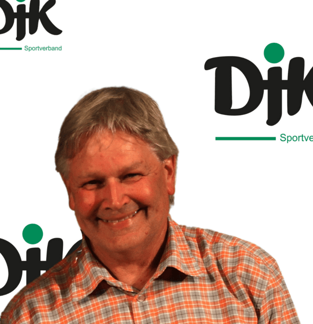 L&auml;chelnder Mann mit grauem Haar, orange-karierter Hemd, vor einem Hintergrund mit dem Logo des Sportverbands Dijk.