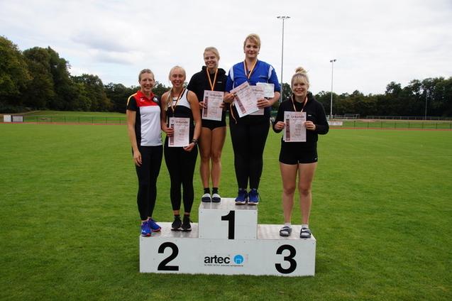 Sechs Athletinnen stehen auf dem Siegerpodest mit Medaillen und Urkunden auf einer Sportanlage.