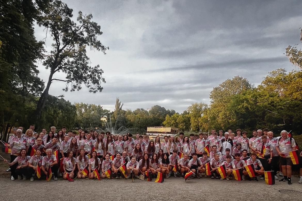 Gruppenfoto von &uuml;ber 100 Menschen im Freien, viele halten Flaggen mit deutschen Farben, vor einem park&auml;hnlichen Hintergrund.