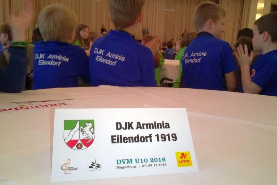 Tischschild mit der Aufschrift &bdquo;DJK Arminia Eilendorf 1919&ldquo; vor Kindern in blauen T-Shirts bei einer Veranstaltung.