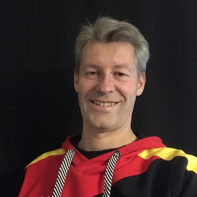 Ein Mann mit grauen Haaren tr&auml;gt einen roten Kapuzenpullover mit den Farben der deutschen Flagge vor schwarzem Hintergrund.