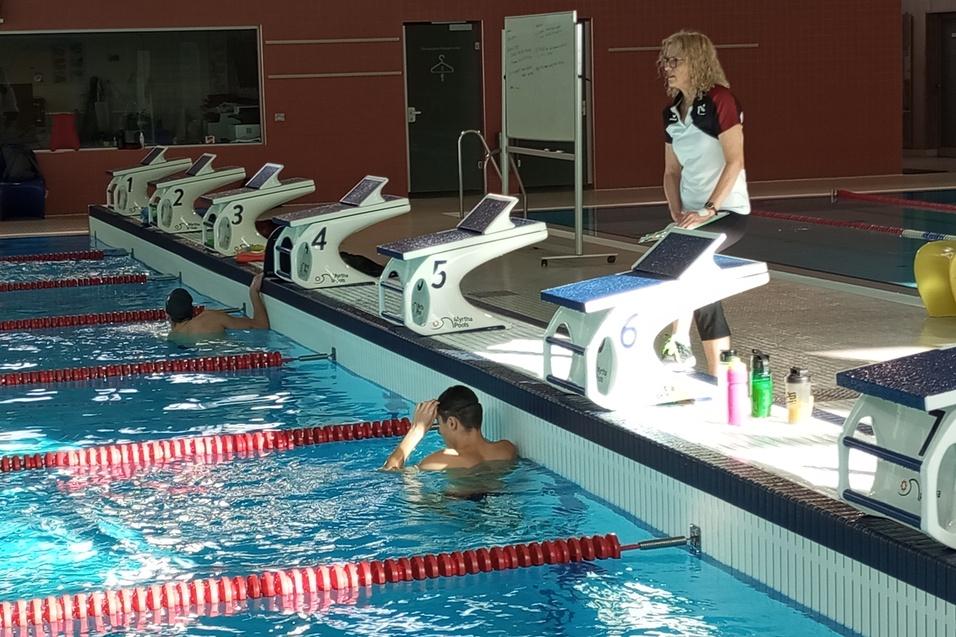 Ein Schwimmbecken mit mehreren Startbl&ouml;cken; ein Trainer beobachtet einen schwimmenden Athleten.
