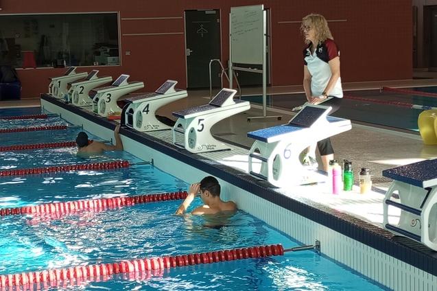 Ein Schwimmbecken mit mehreren Startbl&ouml;cken; ein Trainer beobachtet einen schwimmenden Athleten.