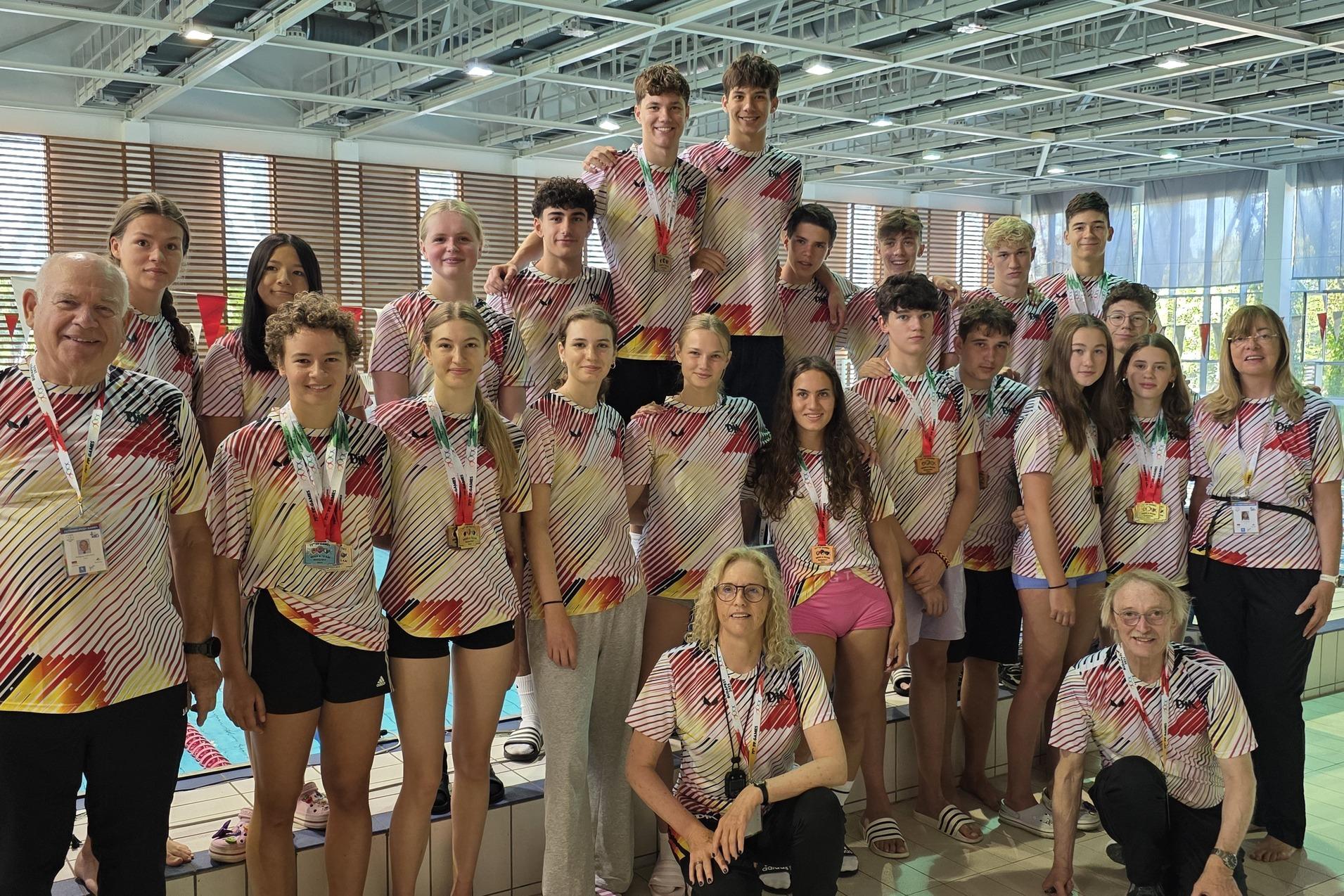 Gruppenfoto von Schwimmern und Trainern am Schwimmbecken, alle tragen einheitliche, gestreifte Shirts.