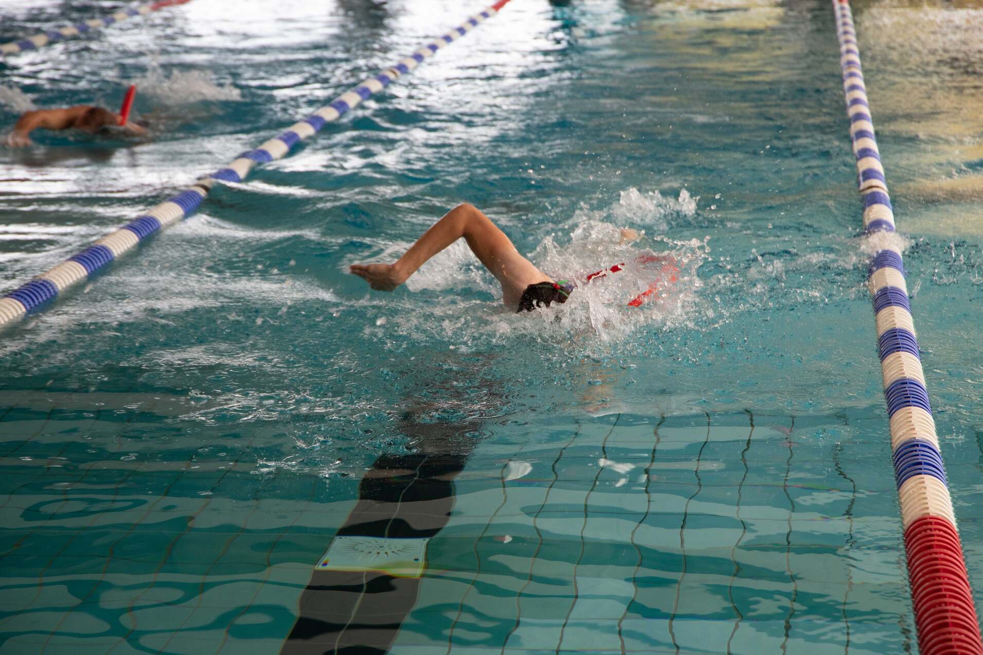 Ein Schwimmer f&uuml;hrt einen R&uuml;ckenschwimmzug in einem Schwimmbecken mit bunten Bahnmarkierungen aus.