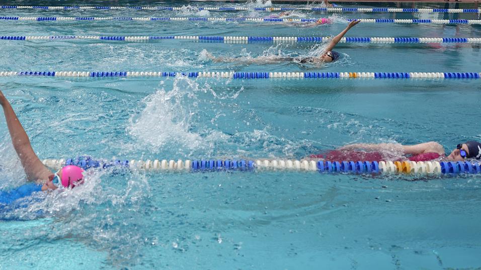 Wettkampf im Schwimmen mit mehreren Teilnehmern und Zuschauern am Beckenrand in einem Wettkampfschwimmbad.