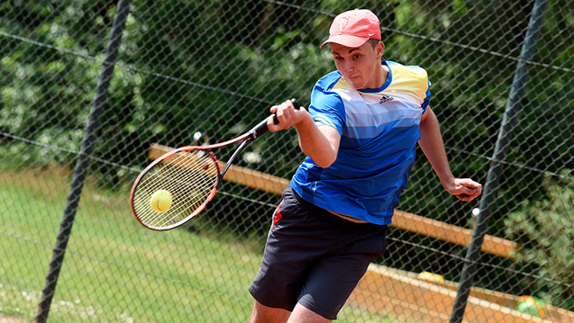 Junger Tennisspieler in blauer Sportbekleidung schl&auml;gt einen Ball auf einem Tennisplatz.