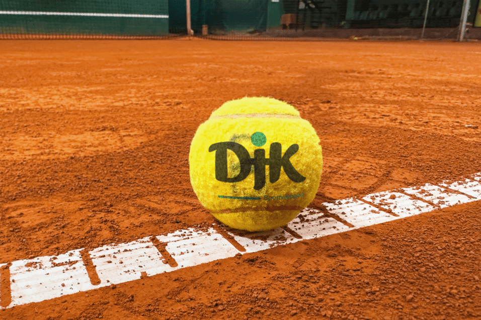 Nahaufnahme eines Tennisballs auf einem roten Sandplatz, teilweise auf einer wei&szlig;en Linienmarkierung.