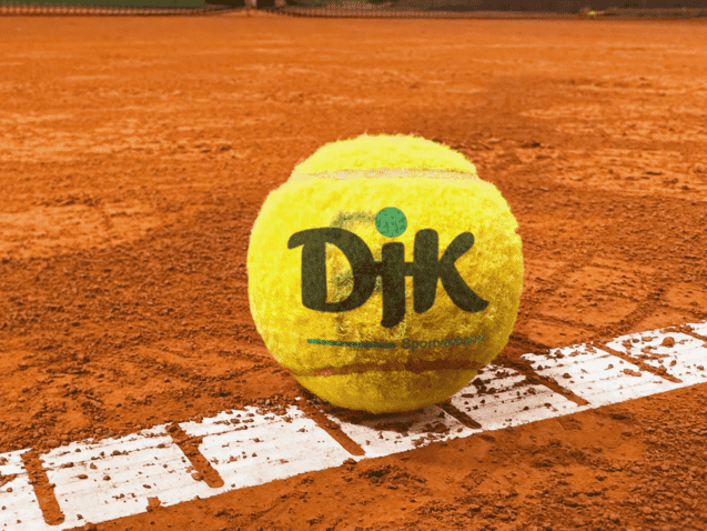 Nahaufnahme eines Tennisballs auf einem roten Sandplatz, teilweise auf einer wei&szlig;en Linienmarkierung.