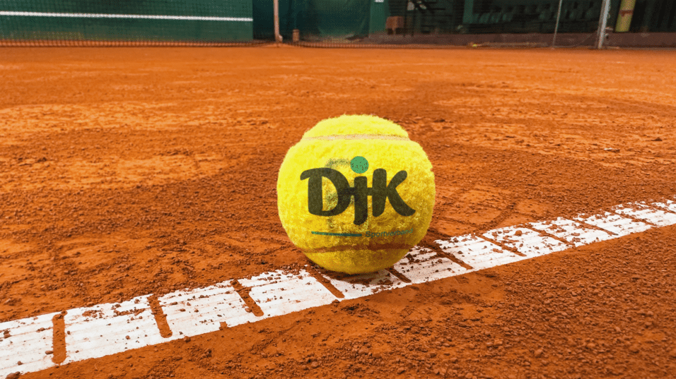 Nahaufnahme eines Tennisballs auf einem roten Sandplatz, teilweise auf einer wei&szlig;en Linienmarkierung.