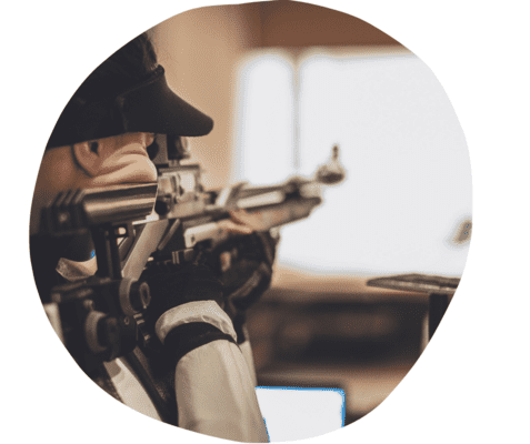 Nahaufnahme einer Person, die mit einem Luftgewehr auf ein Ziel zielt, in einem schlichten Trainingsraum.