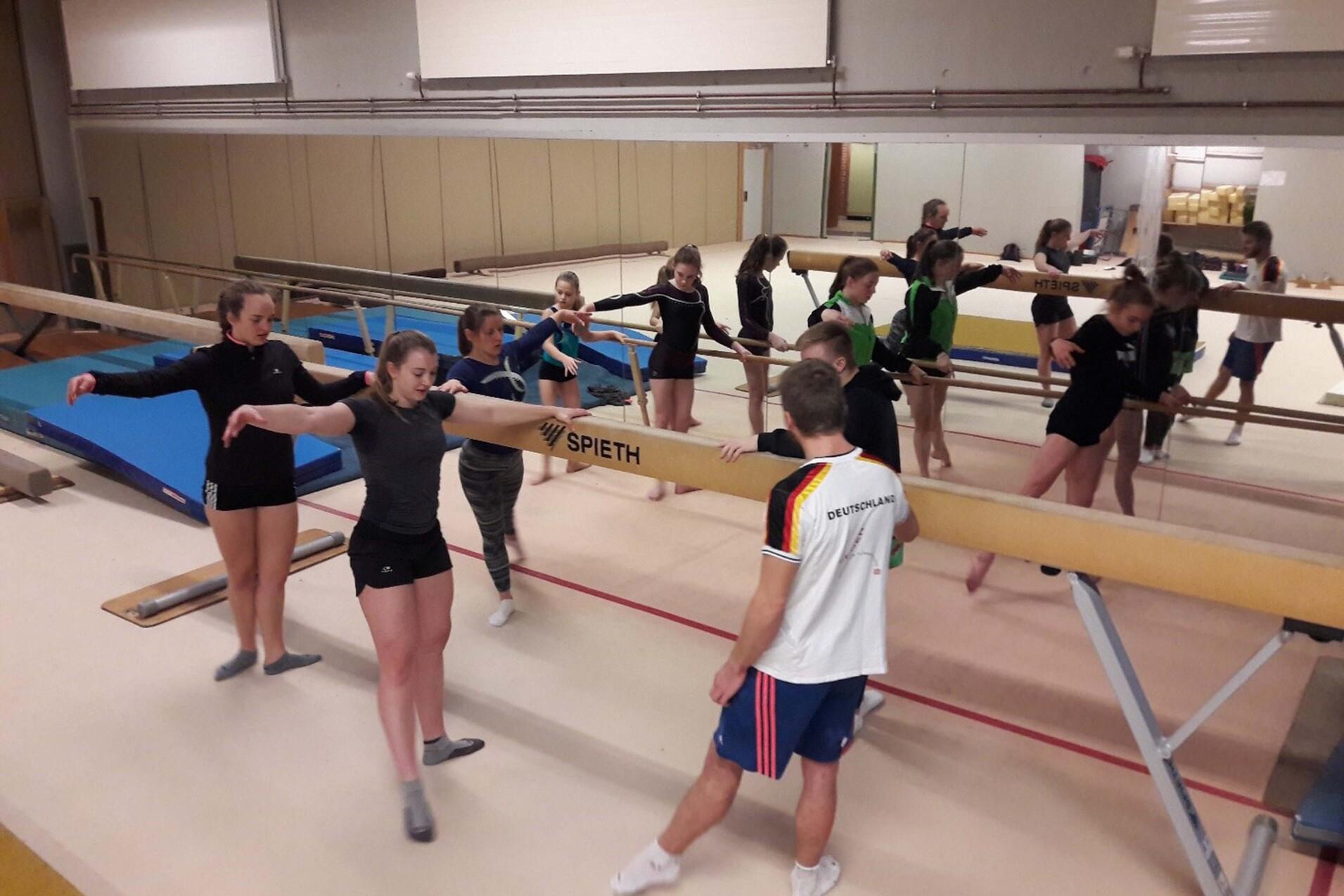 Gruppentraining von weiblichen Turnerinnen an einem Schwebebalken in einer Gymnastikhalle, mehrere &Uuml;bungspaarungen.