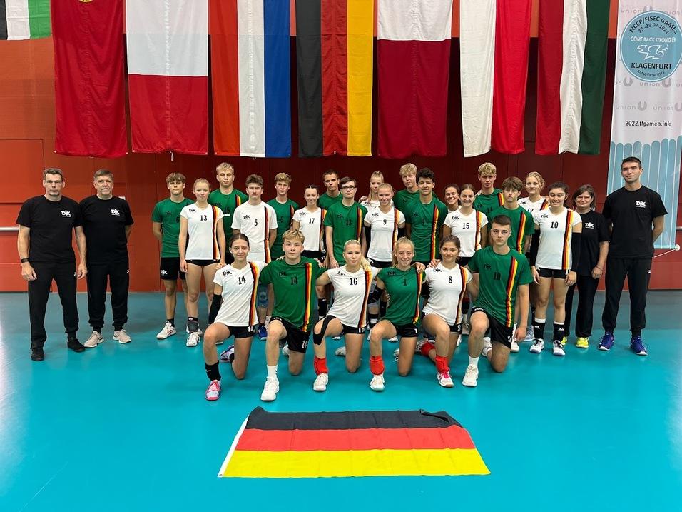 Gruppenfoto von Jugend-Volleyballspielern in Uniformen, mit Fahne Deutschlands und Fahnen im Hintergrund.