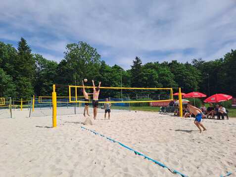 Zwei M&auml;nner springen am Netz beim Beachvolleyballspiel auf einem Sandplatz, um den Ball zu blocken.