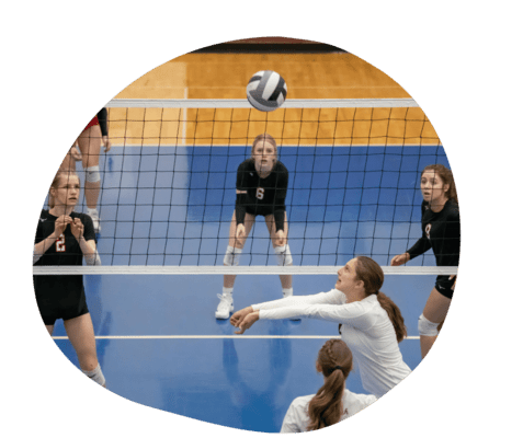 Volleyballspiel mit mehreren Spielerinnen, eine Spielerin in Wei&szlig; bereitet sich auf einen Aufschlag vor.