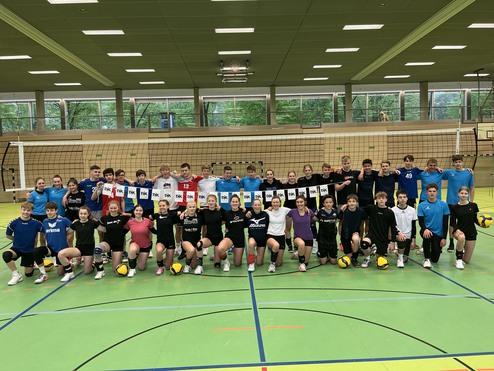 Gruppenshot von Jugendlichen in Sportkleidung mit Volleyball zwischen den Netzen in einer Sporthalle.