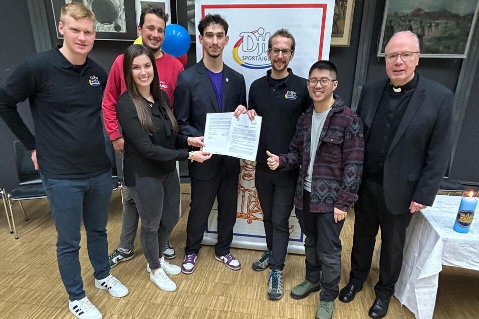 Gruppenfoto mit sechs Personen, die eine Urkunde in der Mitte halten, vor einem Banner mit dem Schriftzug &bdquo;Dill&ldquo;.