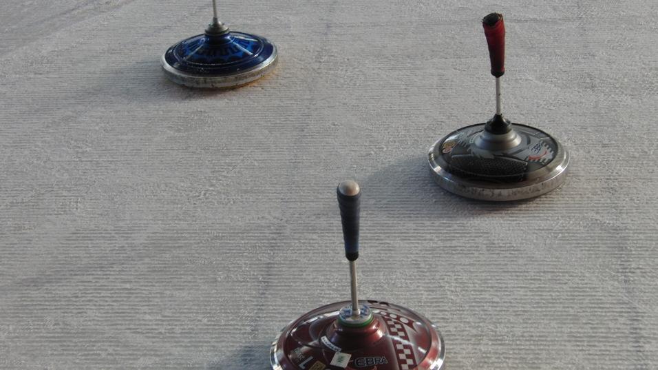 Drei bunte Kreisel stehen auf einem glatten, hellen Untergrund.