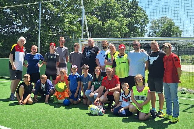 Gruppe von Fu&szlig;ballspielern unterschiedlichen Alters posiert auf einem Kunstrasenplatz vor dem Tor.