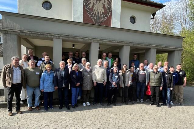 Gruppenfoto von ca. 40 Personen vor einem Geb&auml;ude mit einem Wappen im Hintergrund an einem sonnigen Tag.