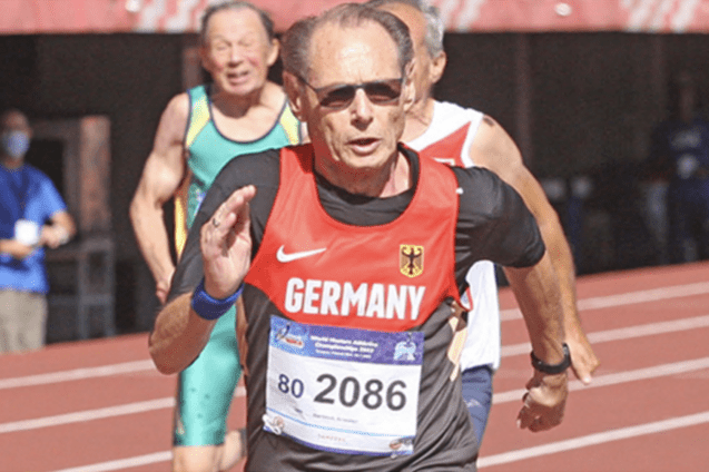 L&auml;ufer mit Startnummer 2086 in Deutschland-Trikot sprintet &uuml;ber eine Laufbahn, mit anderen Athleten im Hintergrund.