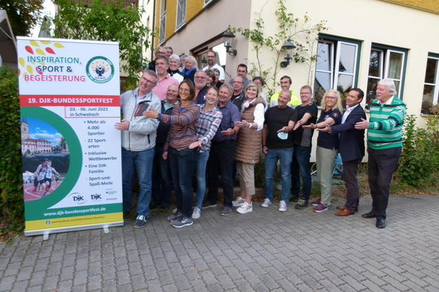 Gruppe von Menschen posiert fr&ouml;hlich vor einem Plakat zum DJK-Bundessportfest in Schwabach.