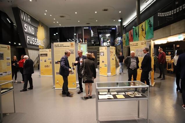 Ausstellung im Fu&szlig;ballmuseum mit Besuchern, Informationsst&auml;nden und einem Glasvitrinen in der Mitte des Raumes.