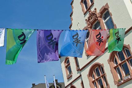 Bunte Fahnen mit chinesischen Schriftzeichen h&auml;ngen vor einem historischen Geb&auml;ude unter blauem Himmel.