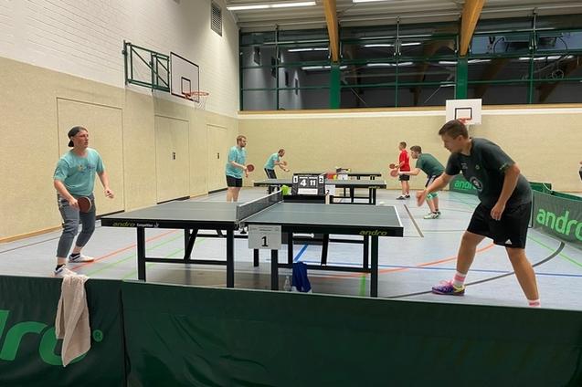Gruppentraining im Tischtennis mit Spielern an mehreren Tischen in einer Sporthalle.