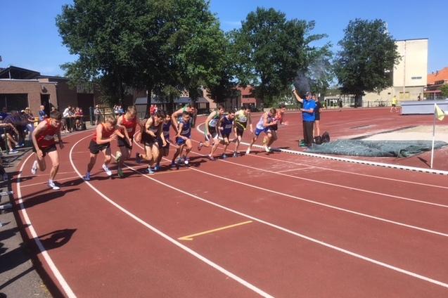 Starterfeld von L&auml;ufern beim Sprintwettbewerb auf einer roten Tartanbahn unter blauem Himmel mit Zuschauern.
