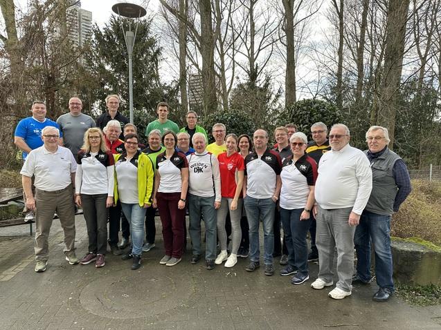 Gruppenfoto von 25 Personen in Sportkleidung, stehend in einem Park mit B&auml;umen und Laternen im Hintergrund.
