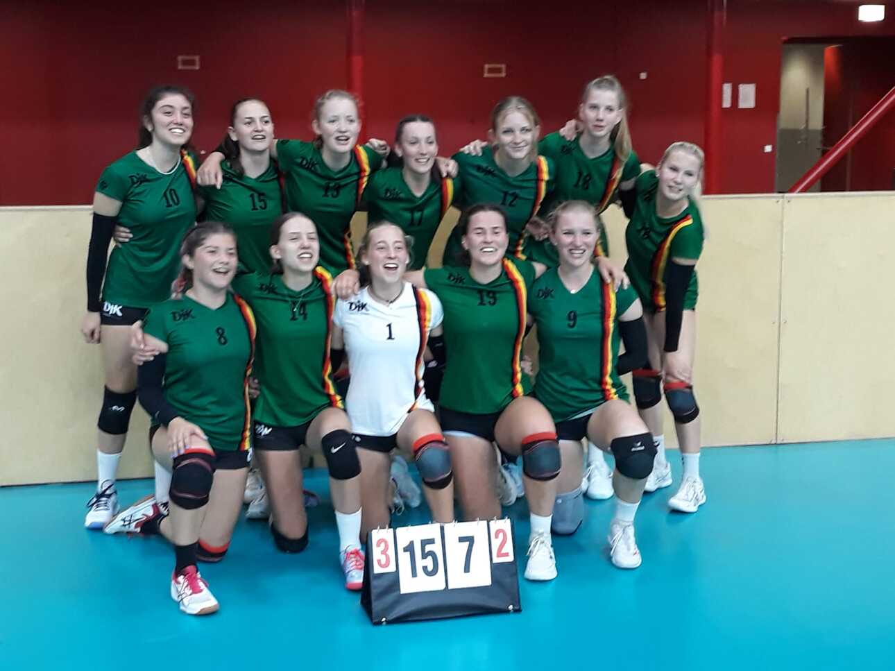 Gruppe von 12 erfolgreichen Volleyballspielerinnen in gr&uuml;nen Trikots, posierend vor einem Spielstand von 15:7.
