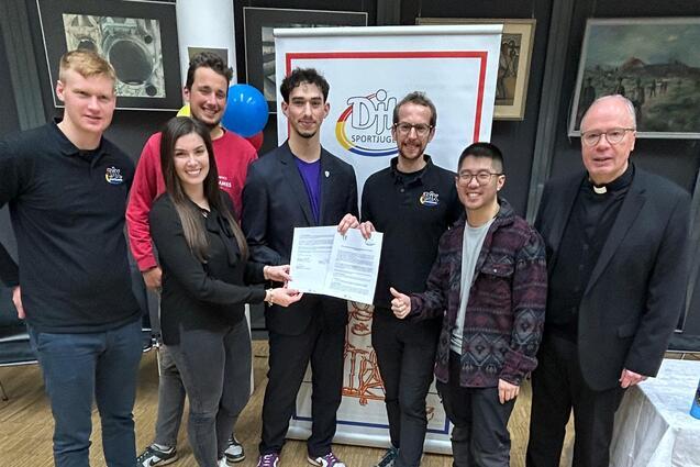 Gruppenfoto mit sechs Personen, die eine Urkunde in der Mitte halten, vor einem Banner mit dem Schriftzug &bdquo;Dill&ldquo;.