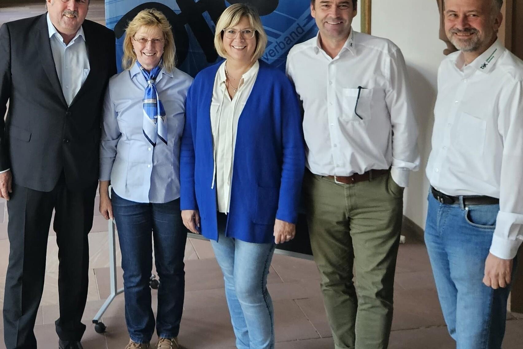 Gruppe von f&uuml;nf Personen in einem Innenraum, posierend vor einem blauen Banner mit dem Logo der Initiative.