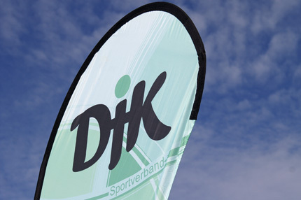 Fahne des DJK Sportverbands mit gr&uuml;nem Hintergrund und schwarzem Logo vor einem blauen Himmel.